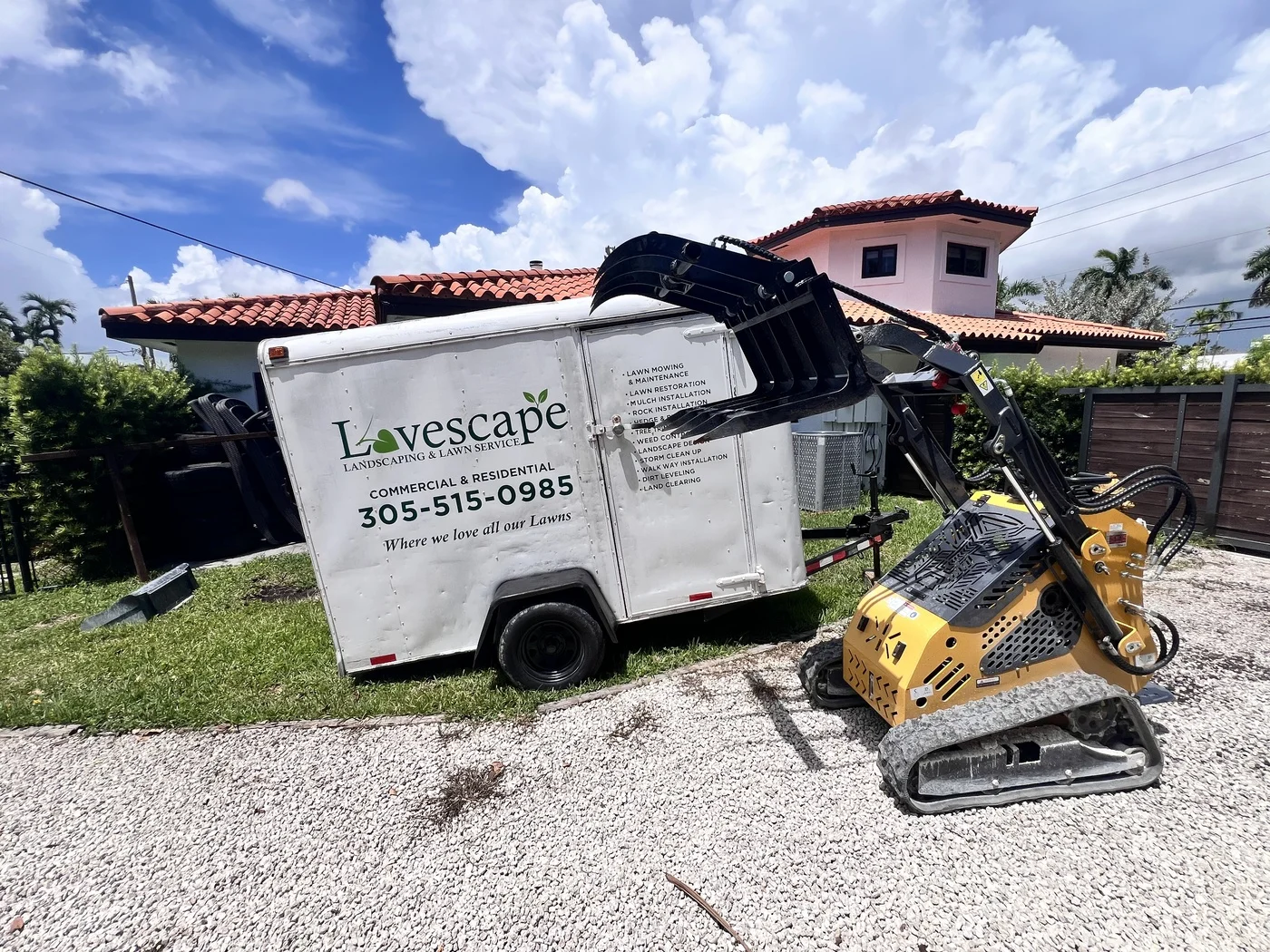 Mini track loader with bucket attachment beside the Lovescape Landscaping trailer in Cutler Bay, FL
